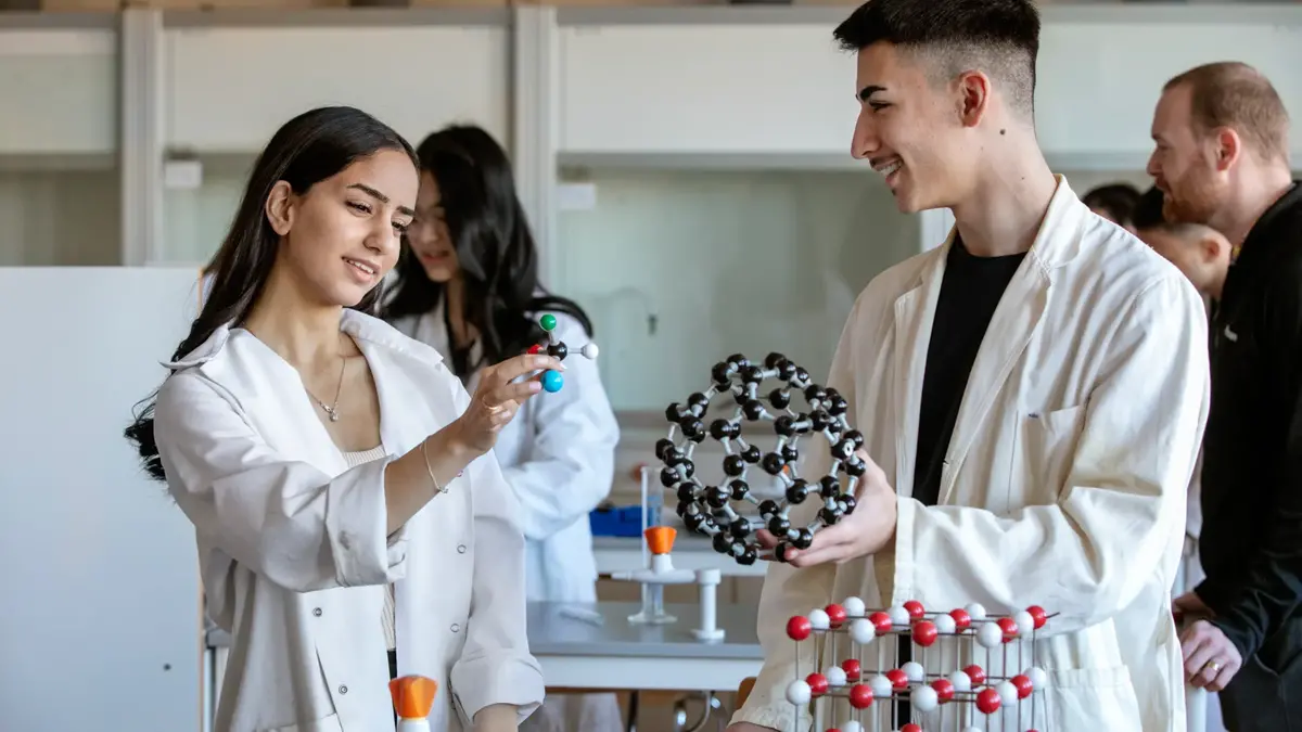 Två elever iklädda vita rockar håller i en molekylmodell och diskuterar.